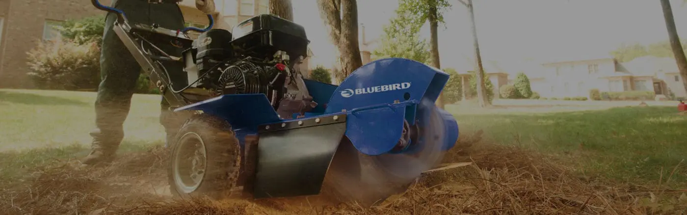 A person using a BlueBird Grinder to grind up mulch in a yard with trees.