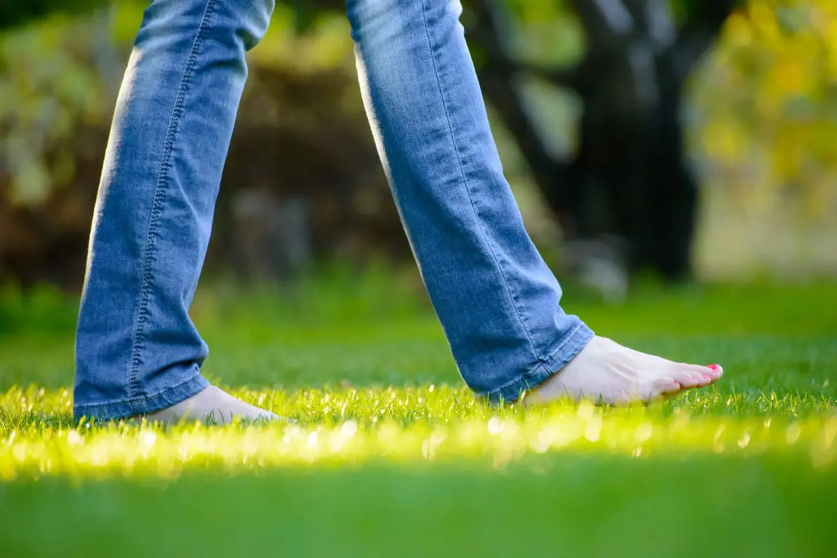 A person walking through a green yard barefoot.